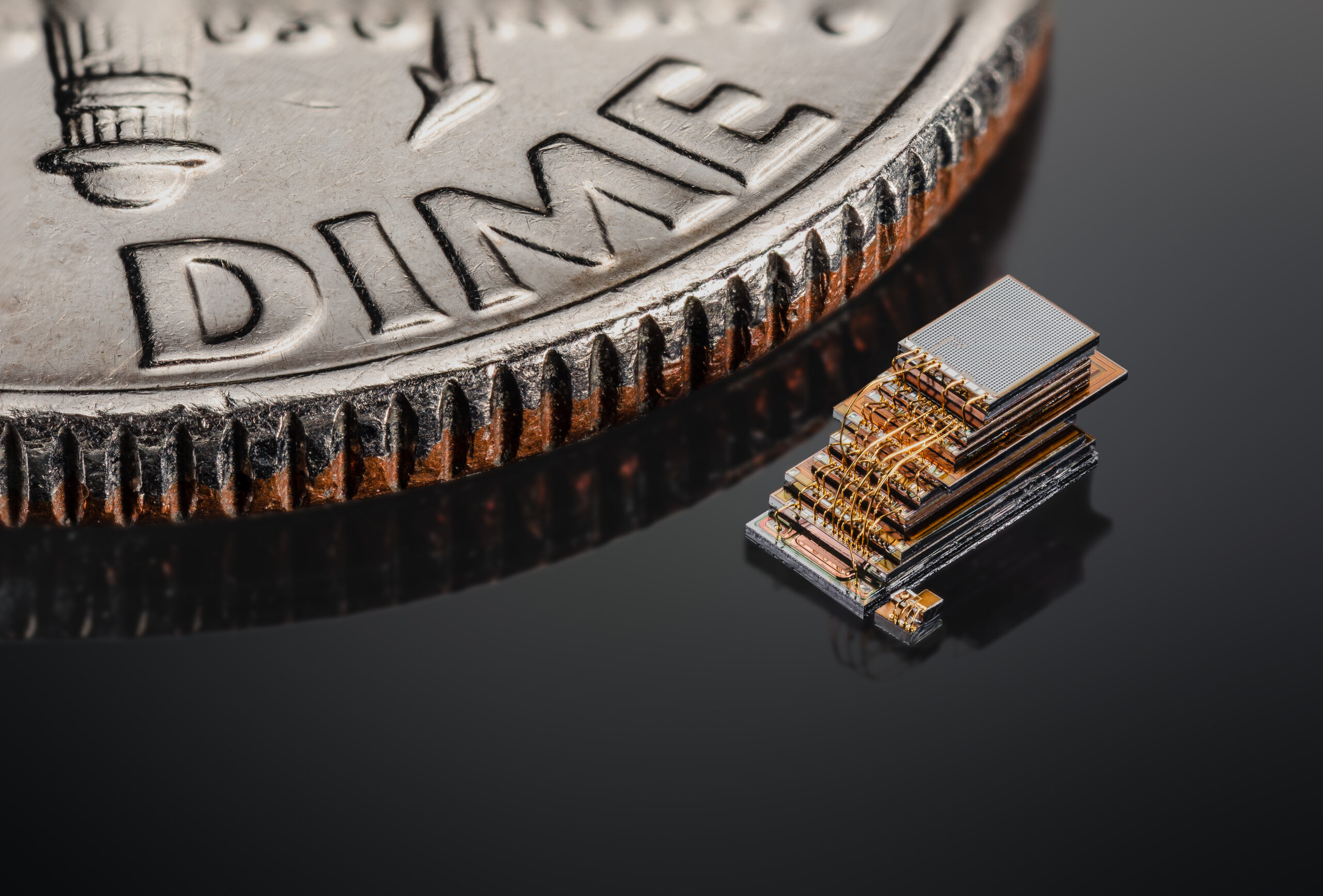 Two tiny computers, looking like stacks of metal components, are next to the edge of a dime.